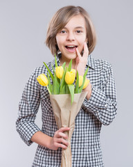 Holidays, Love, Happiness and People concept - Happy Child celebrating Valentines Day. Teen Girl with Flowers. Surprised Girl with bouquet of yellow tulips on gray background.