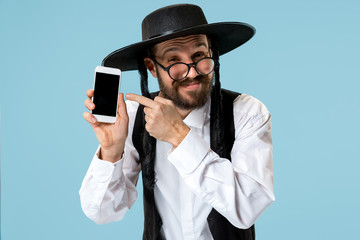 Portrait of a young orthodox Hasdim Jewish man with mobile phone at Jewish festival of Purim at studio. The purim, jewish, festival, holiday, celebration, judaism, pastry, tradition, cookie, religion