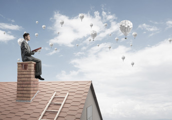 Man on roof reading book and aerostats flying in air