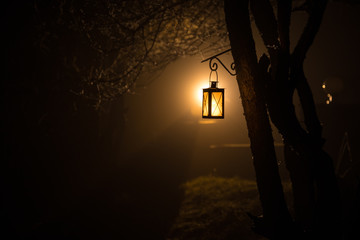 Beautiful colorful illuminated lamp in the garden in misty night. Retro style lantern at night outdoor.