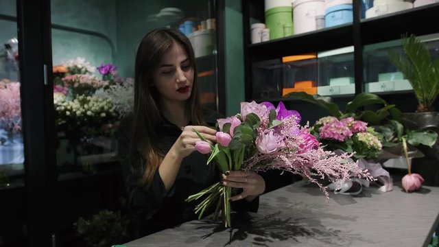 Laughing woman florist makes the bouquet from pink flowers tulips, roses, orchids and solidago.