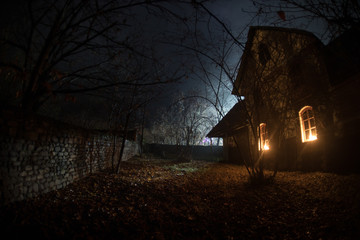 Fototapeta Old house with a Ghost in the forest at night or Abandoned Haunted Horror House in fog. Old mystic building in dead tree forest. Trees at night with moon. obraz