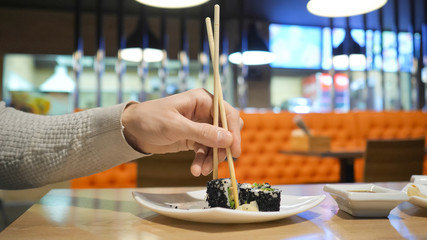 Young guy with chopsticks takes sushi from a plate in a japanese restaurant. Men starts eats japanese food.