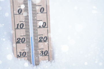 wooden thermometer with falling snow in snow with freezing temperature