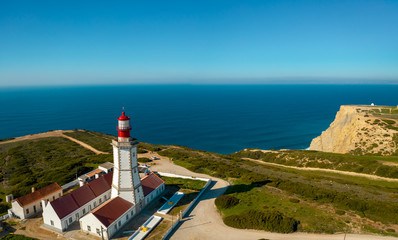 Fototapeta na wymiar Aerial; drone view of white-red lighthouse Cabo Espichel on the edge of the earth; turquoise water of Atlantic ocean stretching to horizon; beautiful portuguese viewpoint with old historic sightseeing