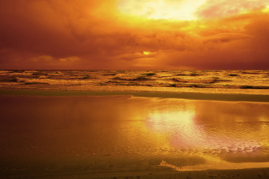 Orange sunset over the stormy sea. Beautiful beach with dramatic sunset sky
