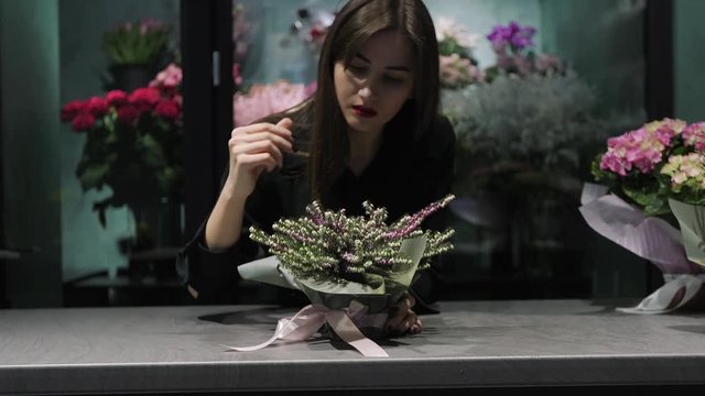 Woman florist in floral shop makes bouquet in pot from Calluna on the table.