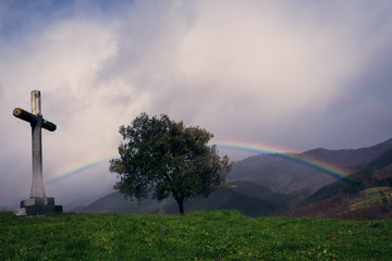 El arco iris sobre un &aacute;rbol y saliendo desde la cruz. El d&iacute;a es nublado con tormentas.