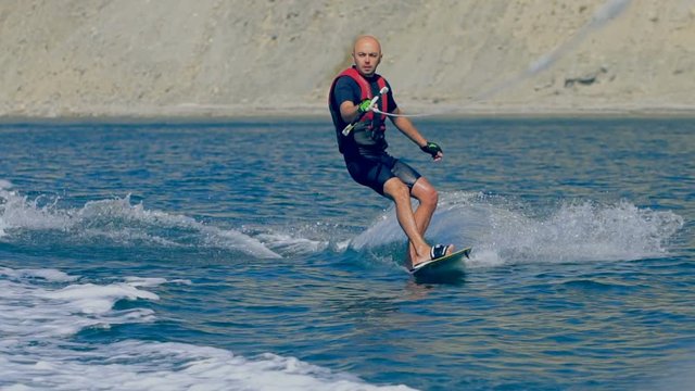 A man wakeboarder clings to a cable and moves behind a boat on the sea. Slow-motion shooting, sport wake board performs tricks on the ocean. Jet ski water sports action shot speeding