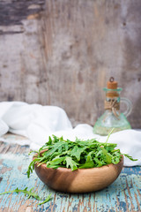 Fresh leaves of arugula in a wooden bowl, jug with oil and napkin on a wooden table. Copy space