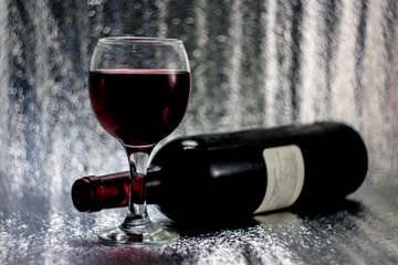Fototapeta premium A glass of red grape wine, a bottle of wine on a silvery blurred bokeh background