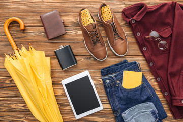 Flat lay with men's clothing, digital tablet and yellow umbrella on wooden background