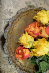 Flat lay 6 roses orange et jaune posées sur un plateau en cuivre