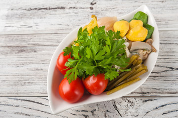 Fermented food in a plate on a white textural wooden table. Cucumbers, zucchini, garlic, marinade, tomatoes, cabbage, ramson, parsley. National Russian food pickles in brine close up and copy space