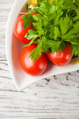 Fermented food in a plate on a white textural wooden table. Cucumbers, zucchini, garlic, marinade, tomatoes, cabbage, ramson, parsley. National Russian food pickles in brine close up and copy space