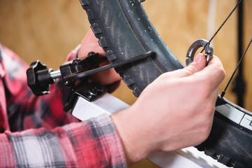 Close-up of men's hands with a specialized wrench on a stand in the workshop tightening the spokes...