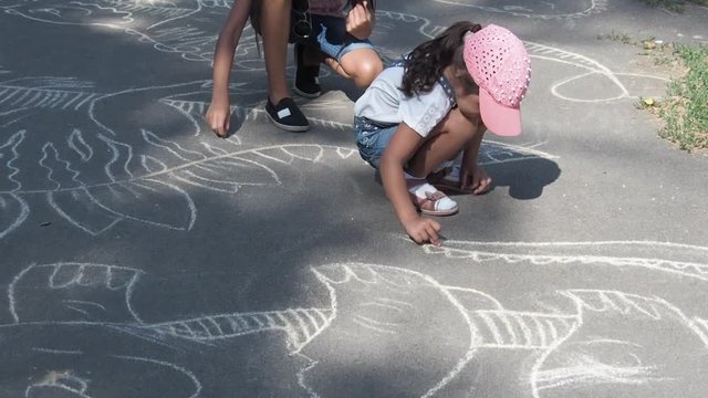 Children are paint on asphalt. Little girls draw with chalk on the asphalt in the park.