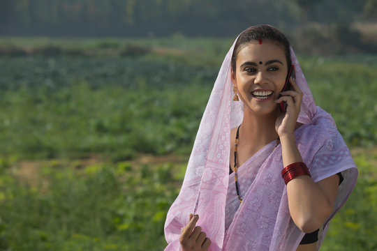 Portrait of a smiling woman standing in an agricultural field with her head covered by saree talking over mobile phone.	 - Powered by Adobe