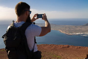 The man photographs an island in the ocean, standing on the edge of a cliff.