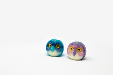 Lucky owl ornament. Small glass lucky object, charm. Blu, azzurro, lilla, viola, giallo. Isolated on white background. Tradition has it that a pair (couple) of owls bring luck.