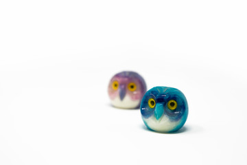 Lucky owl ornament. Small glass lucky object, charm. Blu, azzurro, lilla, viola, giallo. Isolated on white background. Tradition has it that a pair (couple) of owls bring luck.