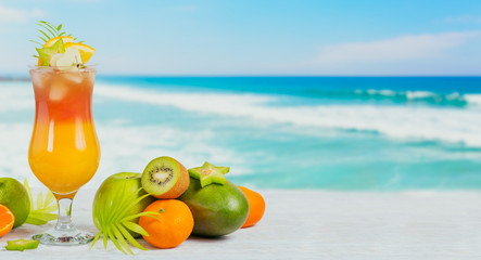 Summer cocktail with various tropical fruits around. Apple, kiwi, tangerine, orange, mango, carambola.