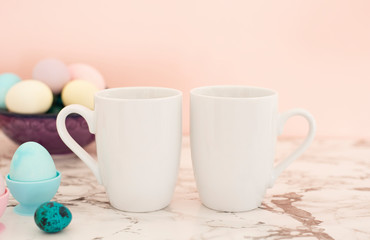 Two White Mugs Mockup - Easter theme. Easter eggs. Colorful eggs in matte colors. Light marble background