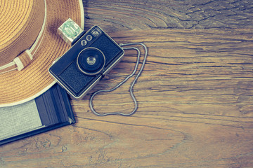 Old compact camera with flash cube, womens hat and black photo album on wooden background. Travel ...