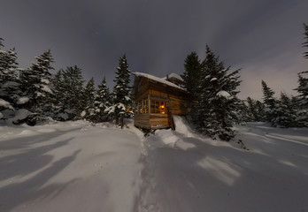 Panorama house chalet during a snowfall in the trees winter forest at night in the moonlight