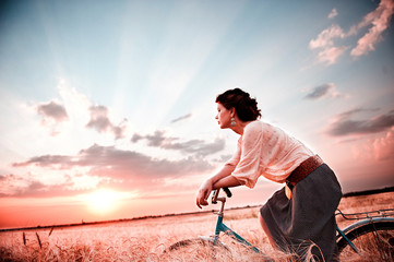 The girl behind the wheel of a bicycle on the background of a sunset in the clouds