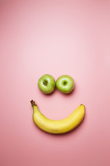 Smiley face with two apples and a banana with copy space on a pink background