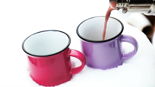 Pouring hot chocolate in the cup. Hot chocolate with marshmallow in pink and violet two cups wrapped in a cozy winter pink scarf on the snow-covered table in the garden.