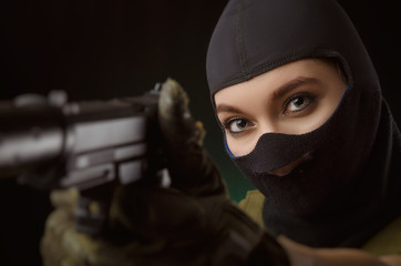 the girl in military special clothes posing with a gun in his hands on a dark background in the haze