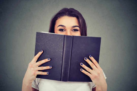 Portrait of a cute young woman hiding behind an open book and looking at camera