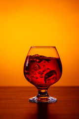 Glass of alcoholic drink Whiskey with ice cubes on wooden table on orange background.