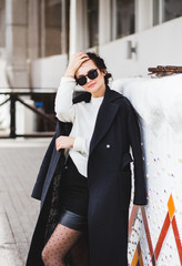 Fashion pretty woman model wearing a dark coat and white sweater, in sunglasses, posing over white background.