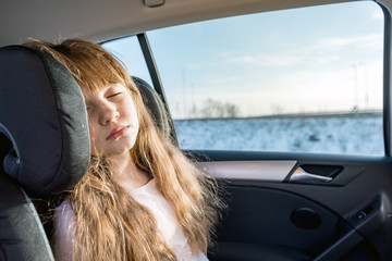 Little girl sitting in car seat and sleeping during long journey