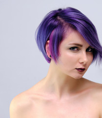 A beautiful, sexy girl with purple hair and a short haircut sits in the middle of the photo with a white background