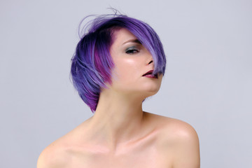 A beautiful, sexy girl with purple hair and a short haircut sits in the middle of the photo with a white background