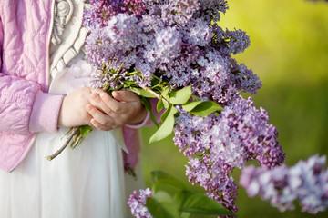 Bouquet of spring lilac flowers in young girls  hands on green background. Close up picture