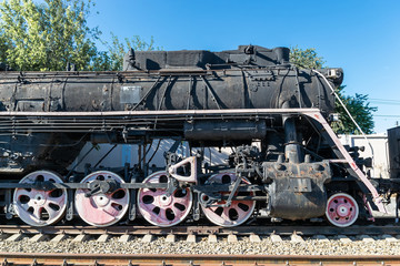 Old rusty steam locomotive beside a railway station platform. Retro train.