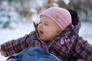 Fröhliches Baby mit rosa Mütze und kariertem Schneeanzug hat Spaß im Schnee