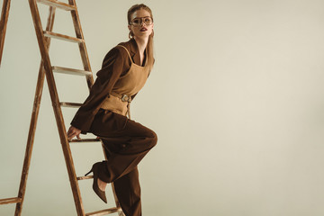 attractive model in retro style posing near wooden ladder isolated on beige