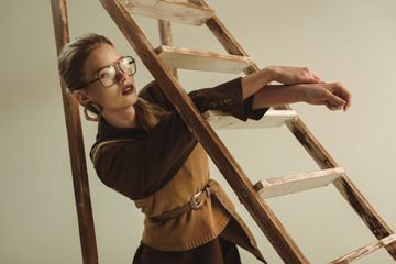 attractive fashionable woman posing near wooden ladder isolated on beige