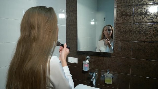 Beautiful young lady in front of mirror and does her makeup. With the help of her brushes applied eyeshadows and blus. Gimbal shot