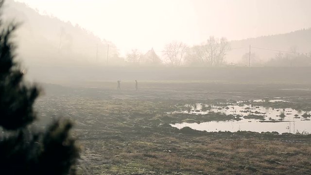 Two workers in the morning fog, go to swampy terrain