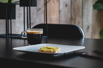 Cup of coffee on a black table with a cracker on a plate for breakfast