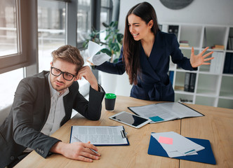 Young woman screaming on man. They are in white meeting room. She stand upon him waving hands and yelling. Guy looks tired and upset.