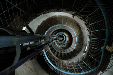 Fototapeta premium Tightly winding cement spiral staircase inside of a lighthouse with a blue railing perspective looking down from the top
