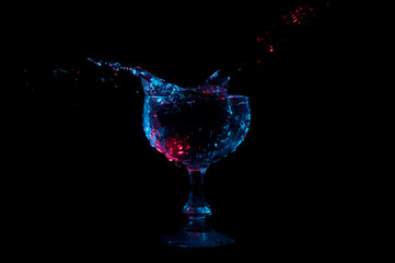 Water splashing out of a goblet shaped glass under red and blue lights on a black background